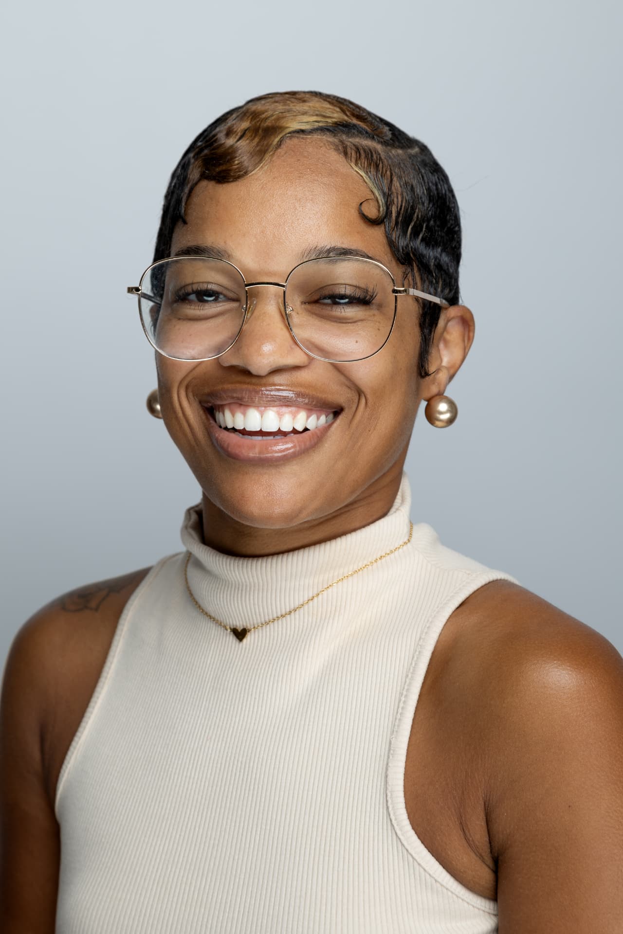 Jay Patrice, founder of Birthday Village, smiling and wearing glasses and a cream sleeveless turtleneck.